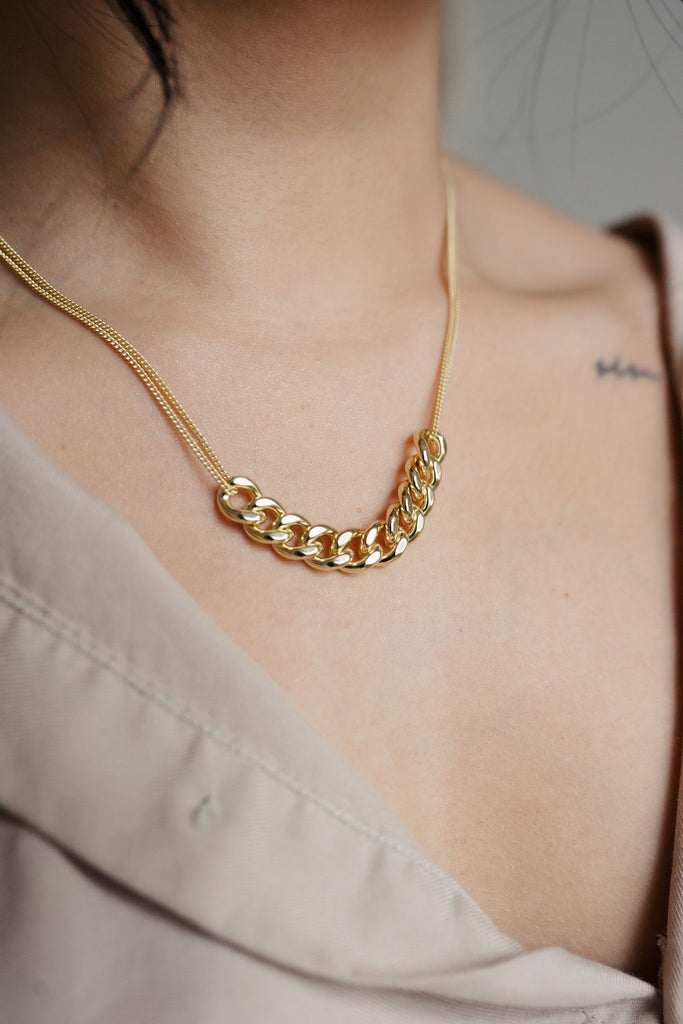 A stunning 14K gold necklace with double strands. The center of the necklace showcases ten larger link chains elegantly joined together, creating a bold and captivating focal point. The golden shine and intricate design make it a luxurious and eye-catching accessory.