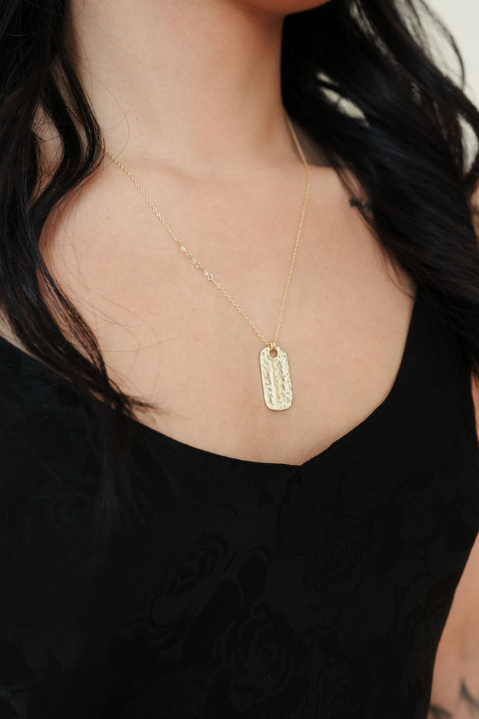 A striking 14K gold necklace with a hammered pendant, beautifully engraved with intricate moon phases. The pendant is adorned with a clear quartz gemstone, suspended on a delicate chain, creating a captivating and celestial-inspired accessory.
