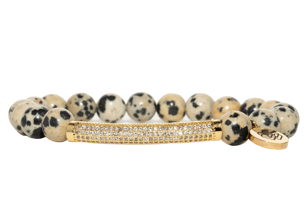 Rhinestone Paved Bar + Dalmatian Jasper Bracelet is plated with gold and cubic zirconia, surrounded with Dalmatian Jasper beads.