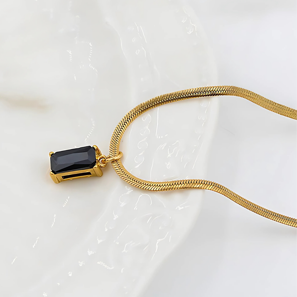 Gold necklace with a black gemstone pendant on a white background