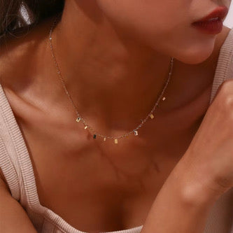 A close-up image of a person wearing a gold-colored choker necklace with multiple small rectangular pendants.