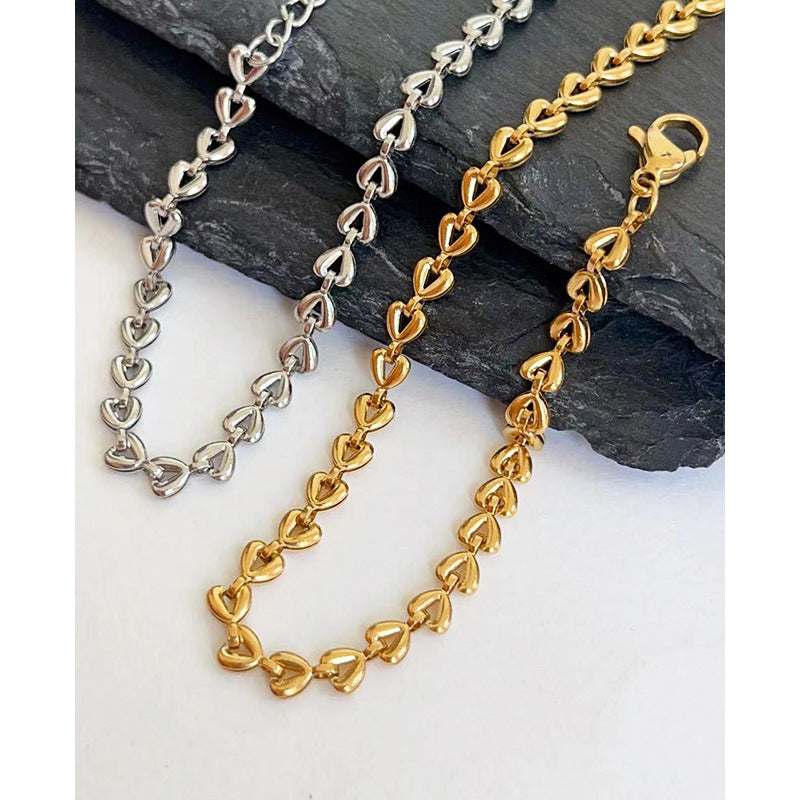 Gold and silver heart-shaped chain necklaces on a stone surface
