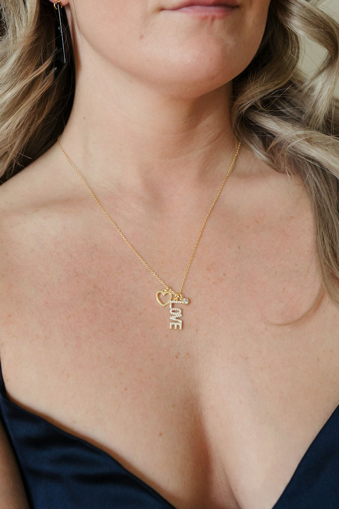 A stunning necklace crafted in 925 sterling silver with 14K gold plating. It features three dainty pendants—a love letter, heart, and round cubic zirconia pendant—creating a charming and elegant accessory