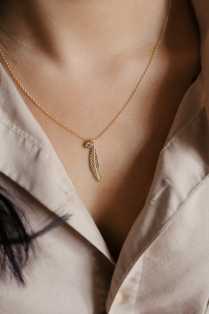 Sterling silver 14k gold necklace featuring an intricate feather design and a clear quartz pendant