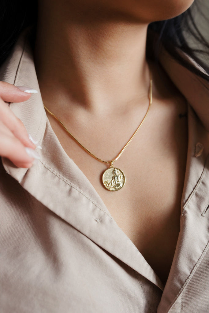 A stunning 14K gold necklace featuring a round pendant showcasing the image of Kuan Yin, the Buddhist goddess of compassion, with intricate details and a radiant golden shine.
